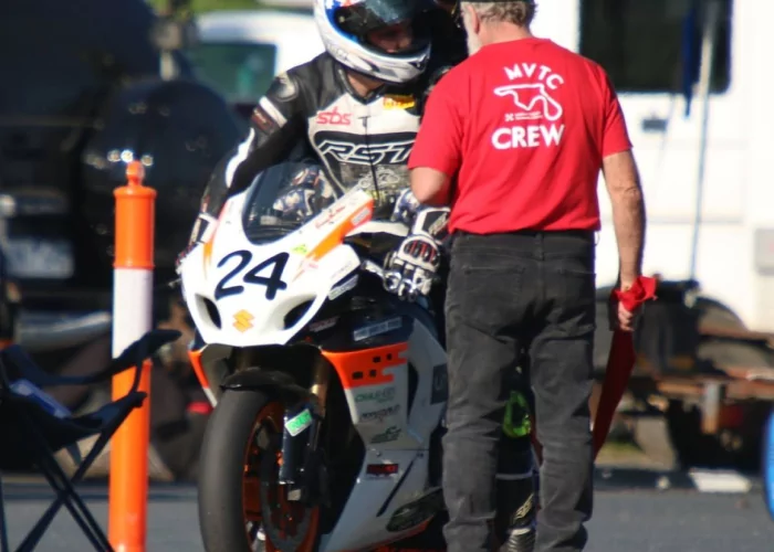 Scrutineer checking a rider’s leathers, helmet, and bike for safety compliance during circuit entry procedure